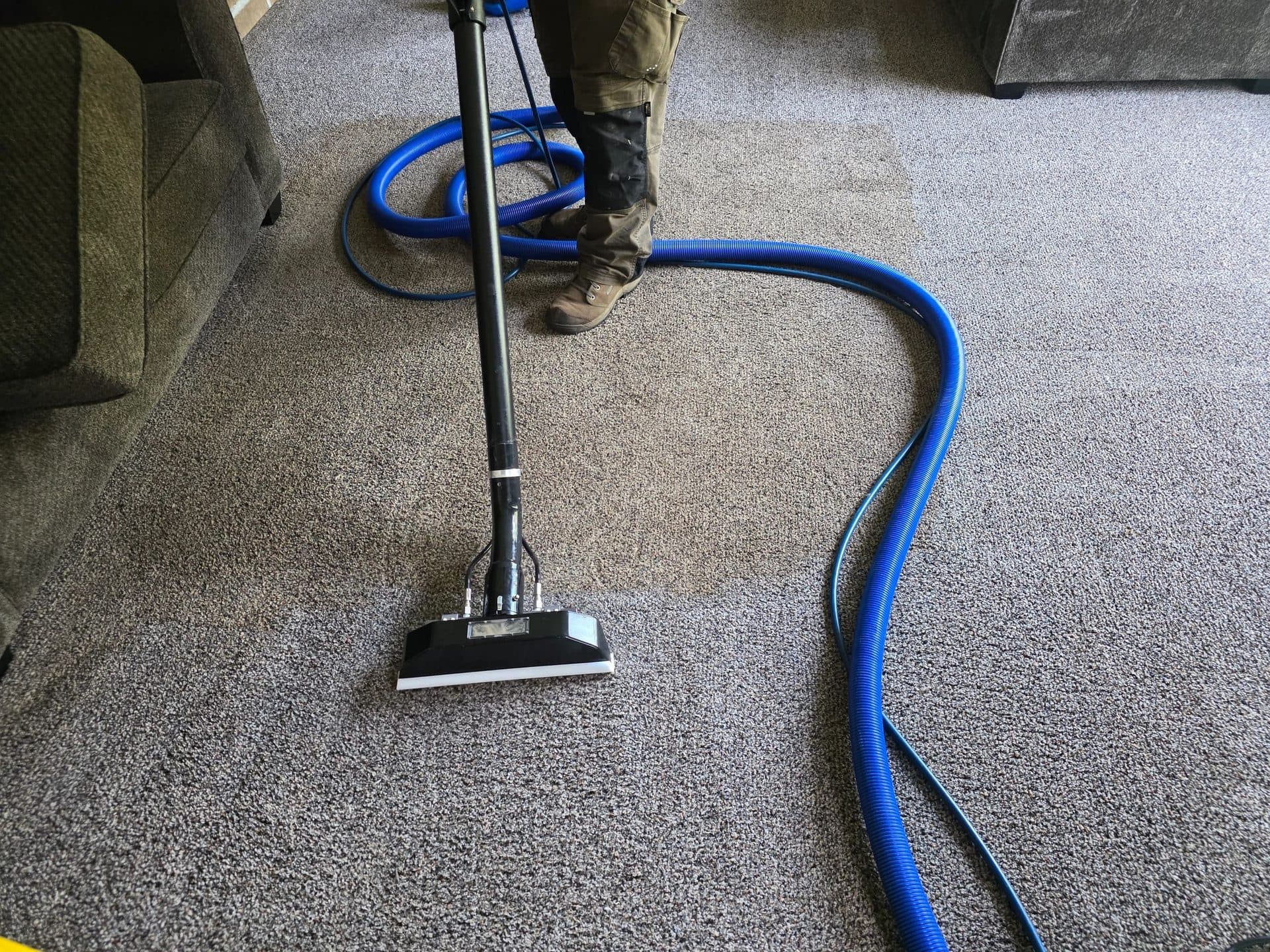 Truck-mounted hot water extraction wand and hose in use on gray carpet