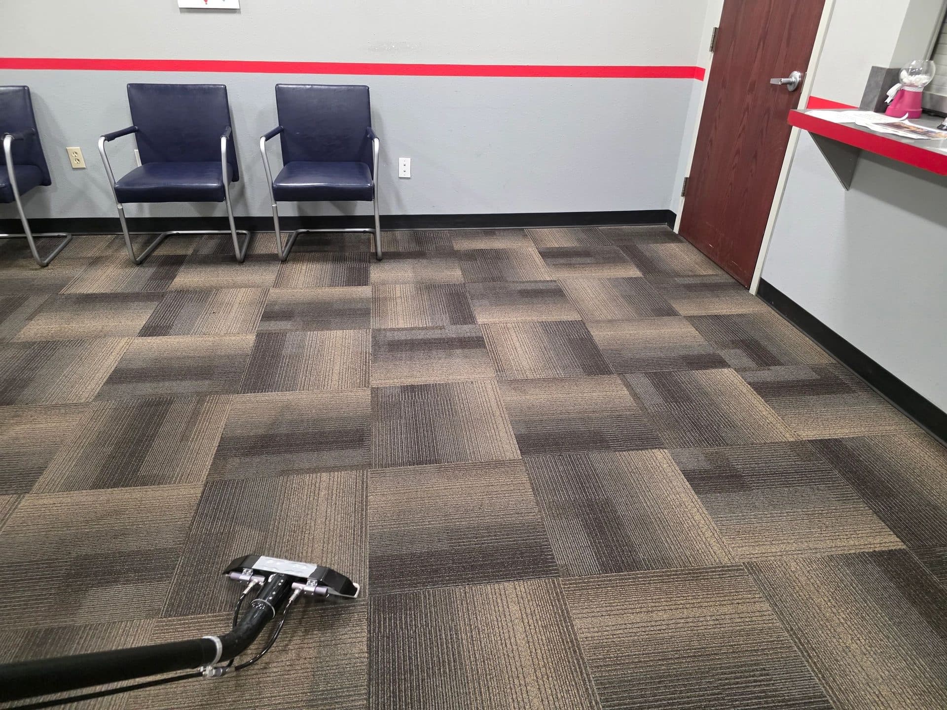 Office waiting room with carpet tiles and a reception counter, with an extraction wand in the foreground