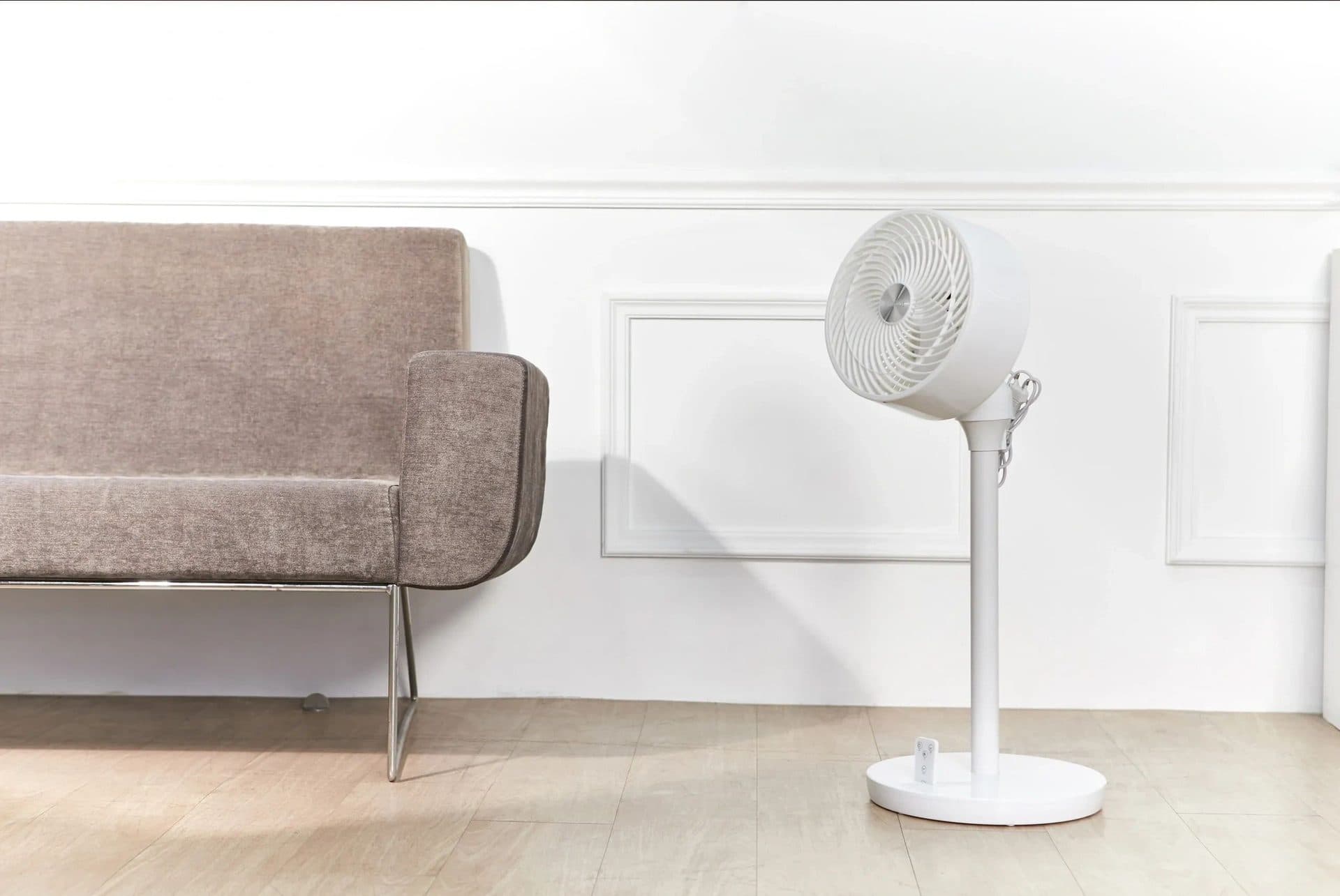 Pedestal fan circulating air beside a fabric sofa